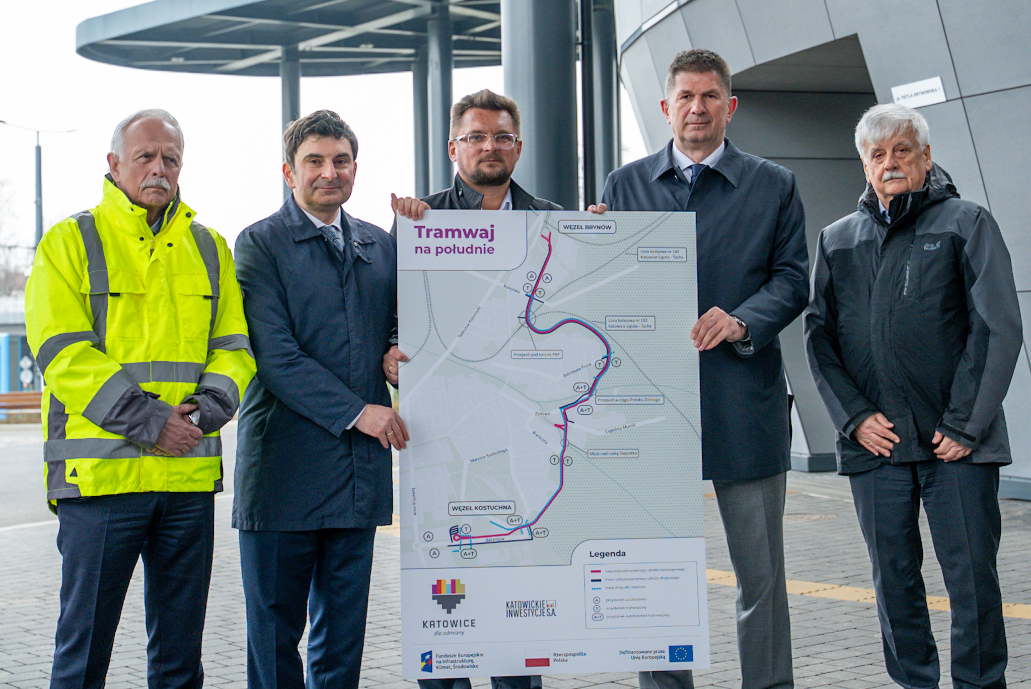 Tablica z nową linią tramwajową. Na drugim planie uczestnicy briefingu prasowego.