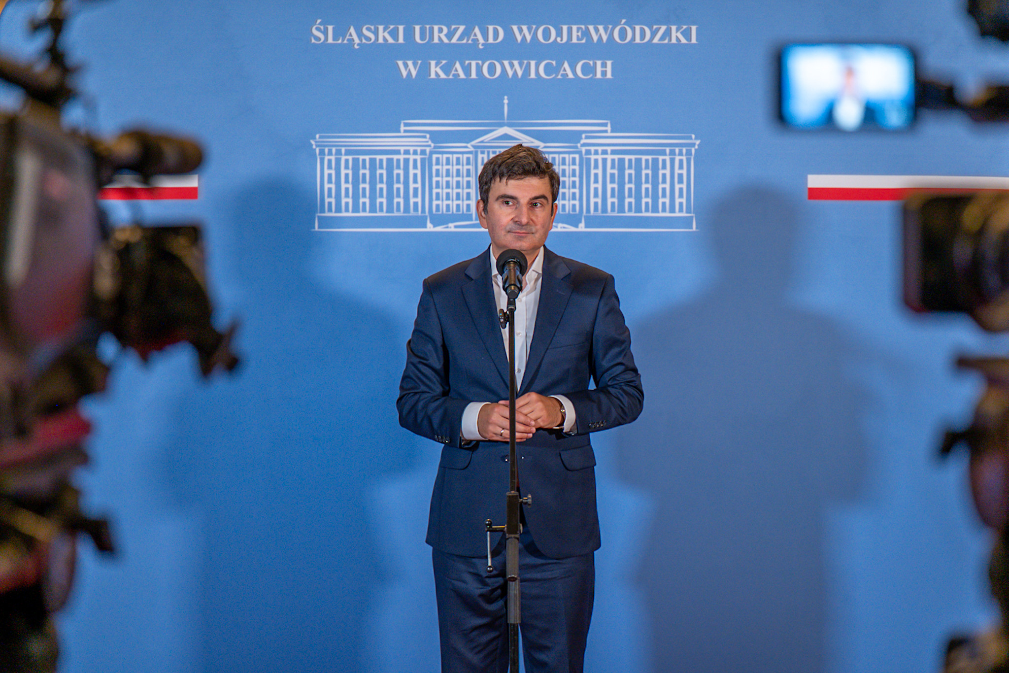 Wojewoda Śląski przed kamerami telewizyjnymi na tle ścianki Śląskiego Urzędu Wojewódzkiego w Katowicach.