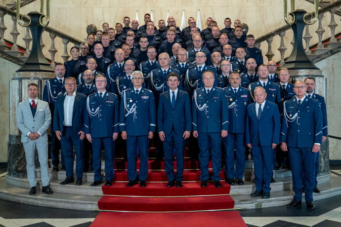 Nowo przyjęci policjanci, kierownictwo śląskiej policji i wojewoda śląski stoją na schodach Westybulu Śląskiego Urzędu Wojewódzkiego w Katowicach ustawienie do zdjęcia grupowego.